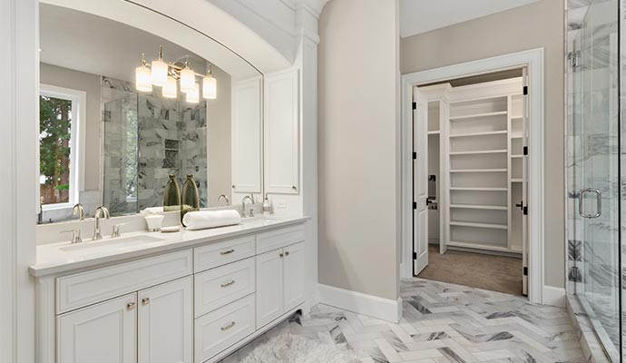 White double sink vanity with arched mirror and open walk in closet in background