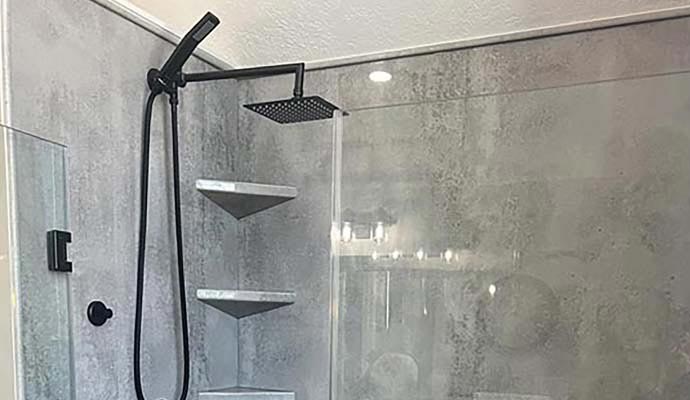 Black rain shower head and handle inside glass shower enclosure with gray walls