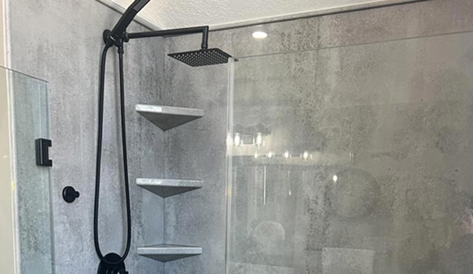 Black rain shower head and handle inside glass shower enclosure with gray walls