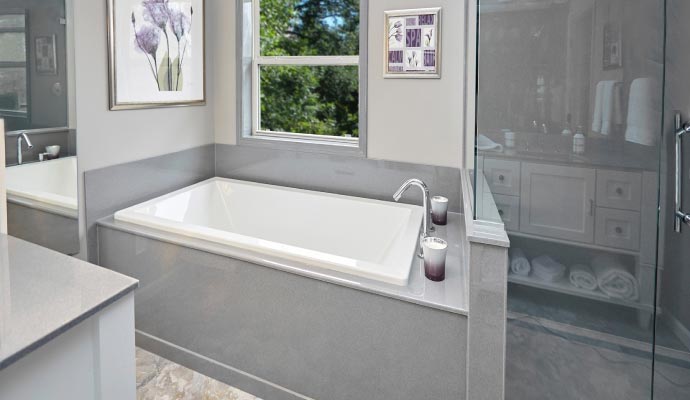 Built in rectangular bathtub under window next to glass shower enclosure