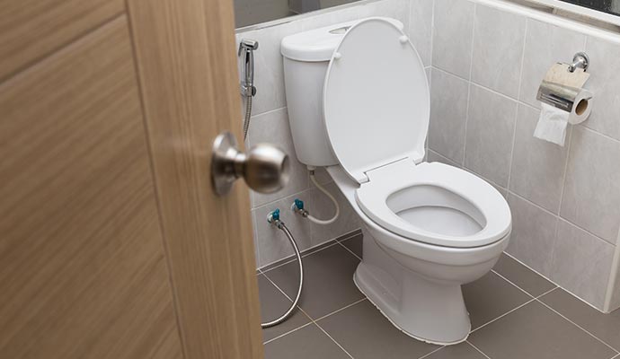 White toilet with open lid handheld bidet spray and tiled walls